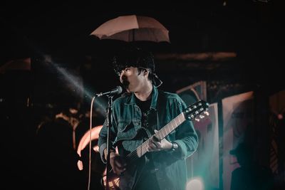 Man singing while playing guitar on stage at night