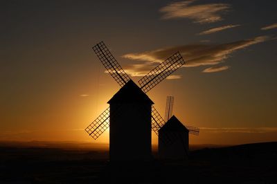 Silhouette of traditional windmills against sky during sunset