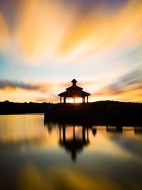 Silhouette built structure in lake against orange sky
