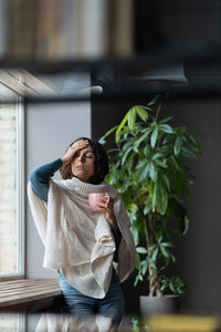 Unhealthy unwell businesswoman having fever touching forehead while drinking hot tea in office