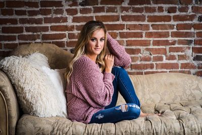 Portrait of young woman sitting against brick wall