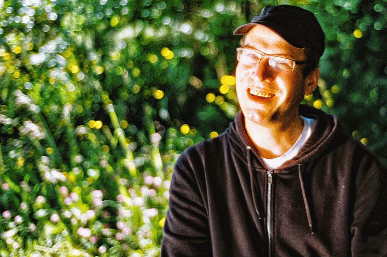 one person, adult, green, portrait, smiling, happiness, men, nature, person, plant, lifestyles, glasses, front view, headshot, emotion, day, outdoors, leisure activity, tree, clothing, sunlight, casual clothing, autumn, cheerful, flower, eyeglasses, spring, standing, smile, teeth, waist up, looking, hat, human face, cap, growth, senior adult, mature adult
