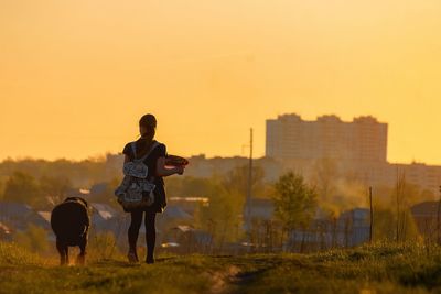 Rear view of father and daughter walking on street against sky during sunset