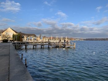 Pier on lake by buildings against sky