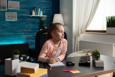 Woman looking away while sitting on table at home