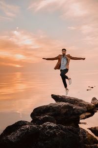 Portrait of man levitating over rock at beach during sunset