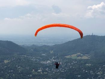 Person paragliding over mountains against sky