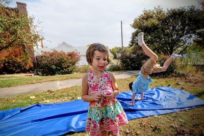 Girl standing against brother practicing handstand on blue fabric at park