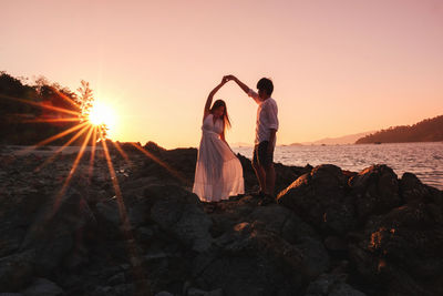 Woman standing on rock by sea against sky during sunset