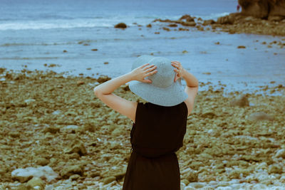 Rear view of woman in hat standing at beach