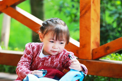 Close-up of cute girl holding backpack sitting in park