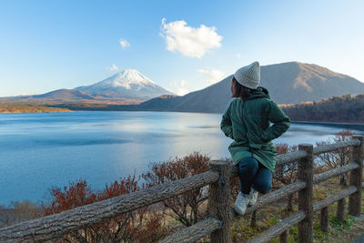 Rear view of man standing on mountain by lake against sky