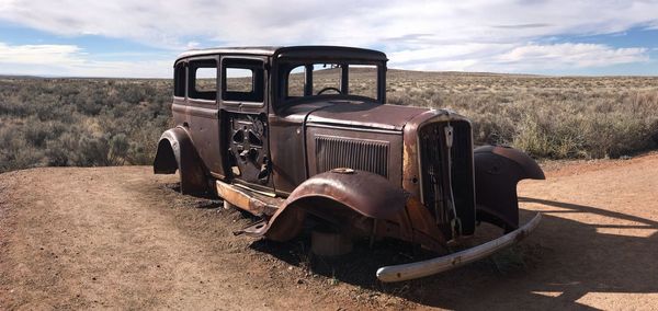 Abandoned vintage car on field against sky