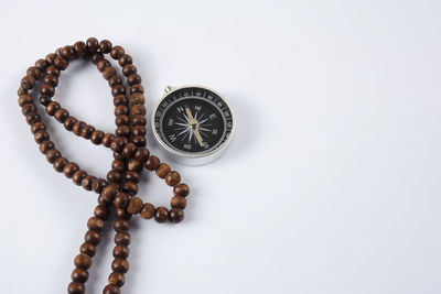 Close-up of compass with bead necklace over white background