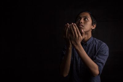 Young man praying against black background