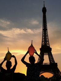 Low angle view of silhouette sibling with balloons near eiffel tower against sky during sunset