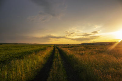 Road amidst field against sky during sunset