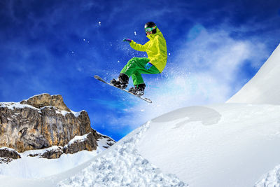 Low angle view of man snowboarding in mid-air above snowcapped mountain