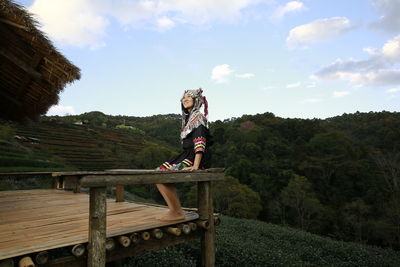 Woman sitting on wood against sky