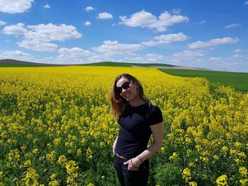 Young woman standing on yellow flowering plants on field against sky