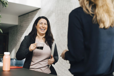 Smiling businesswoman having coffee while talking to colleague at conference