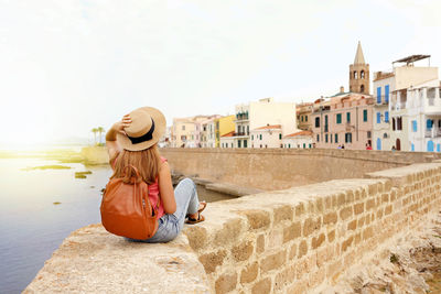 Rear view of woman sitting on wall looking at town