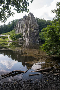 Reflection of trees on rocks in water against sky