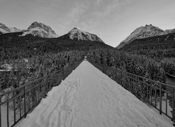 Scenic view of pedestrian bridge by snowcapped mountains against sky