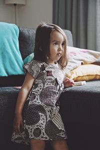 Girl looking away while standing by sofa at home