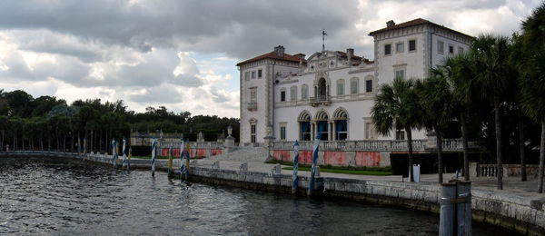 Buildings at waterfront against cloudy sky