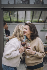 Happy female senior friends with wineglasses greeting each other at dinner party