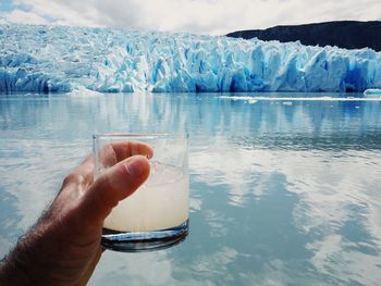 Close-up of hand holding drink against lake during winter