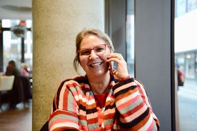 Close-up portrait of cheerful mature woman talking on phone while sitting outdoors