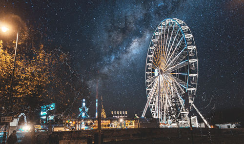 Illuminated ferris wheel against sky in city at night