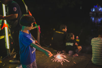 Side view of girl holding illuminated sparkler at night