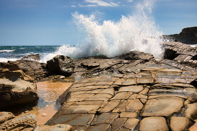 Scenic view of big waves against sky with rocks in foreground