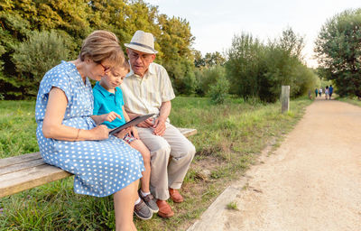 Grandparents with grandson sitting on bench while using digital tablet