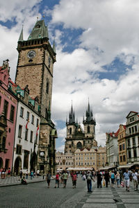 Tourists on city street against cloudy sky