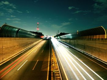 Light trails on road in city against sky at night