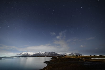 View of lake by snowcapped mountain against sky at night