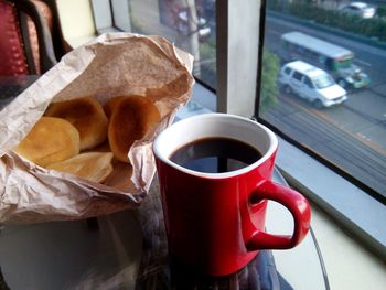 Close-up of black coffee and food by window