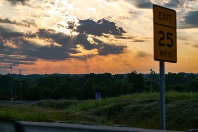 Road sign against sky at sunset