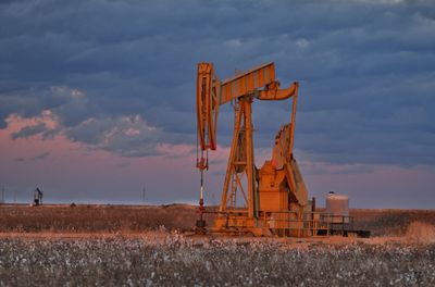 Drilling rig on oil field against cloudy sky during sunset