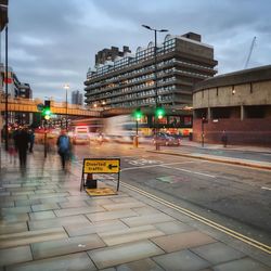 Traffic on road in city against cloudy sky