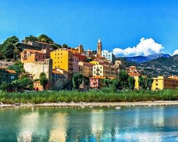 Buildings by lake against blue sky