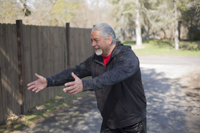 Smiling senior man gesturing while standing on footpath at park