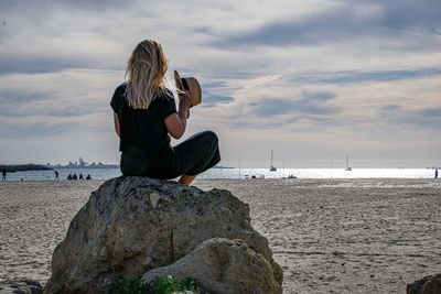 Rear view of woman sitting on rock against sea