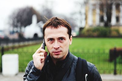 Portrait of man talking on mobile phone while standing against house