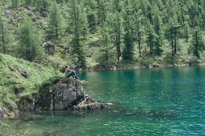 Alone man sits on a stone by the lake and looks at the beauty of nature. calm and unity with nature