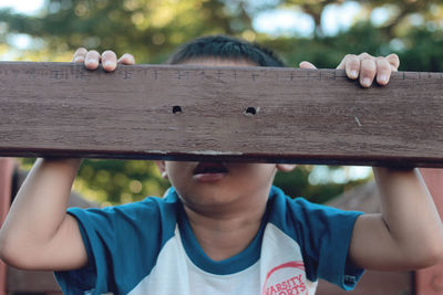 Close-up of boy playing with wooden railing
